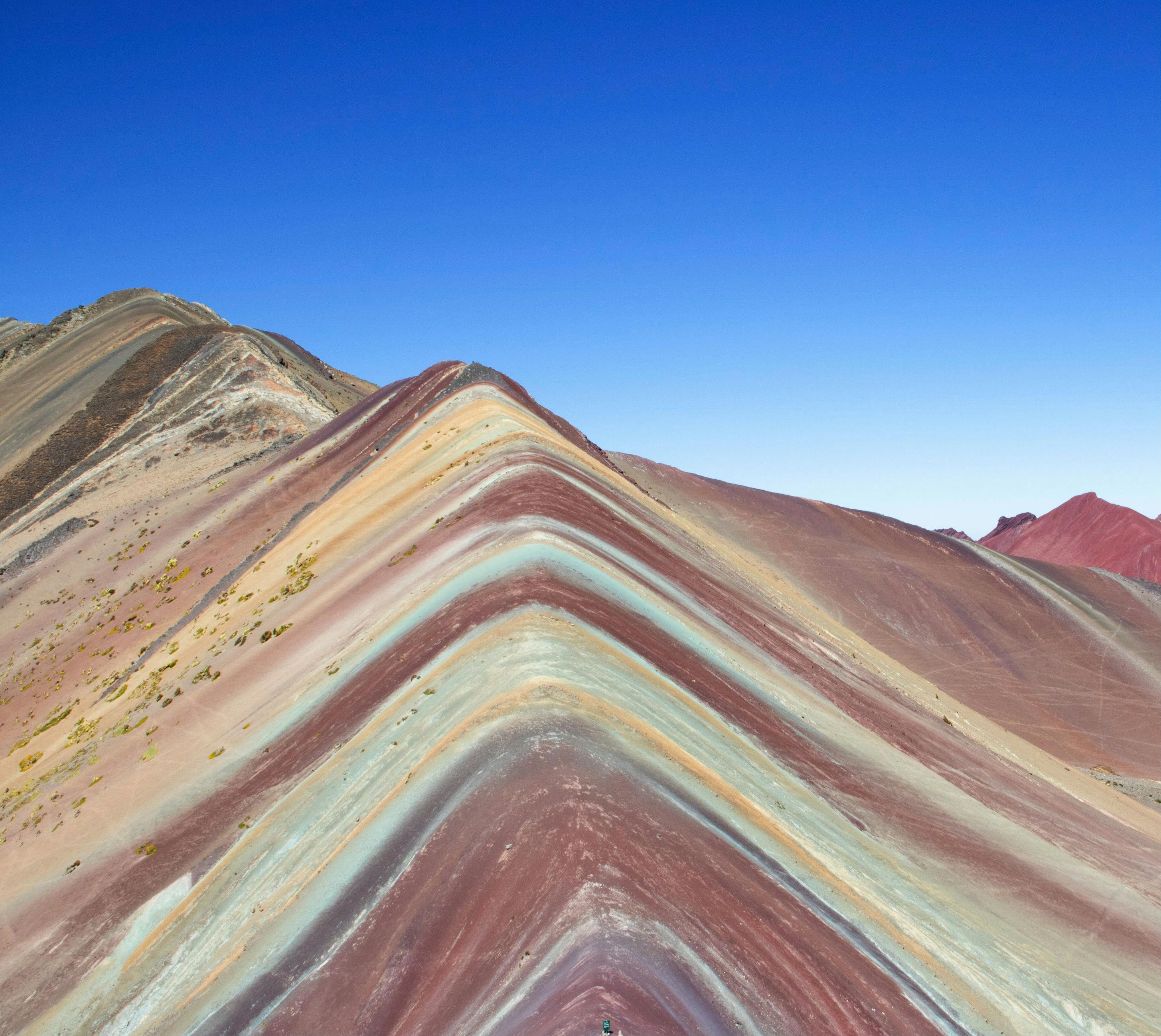 Ένα βουνό με πολύχρωμα ριγέ στρώματα κόκκινου, κίτρινου και μπλε κάτω από έναν καταγάλανο ουρανό.