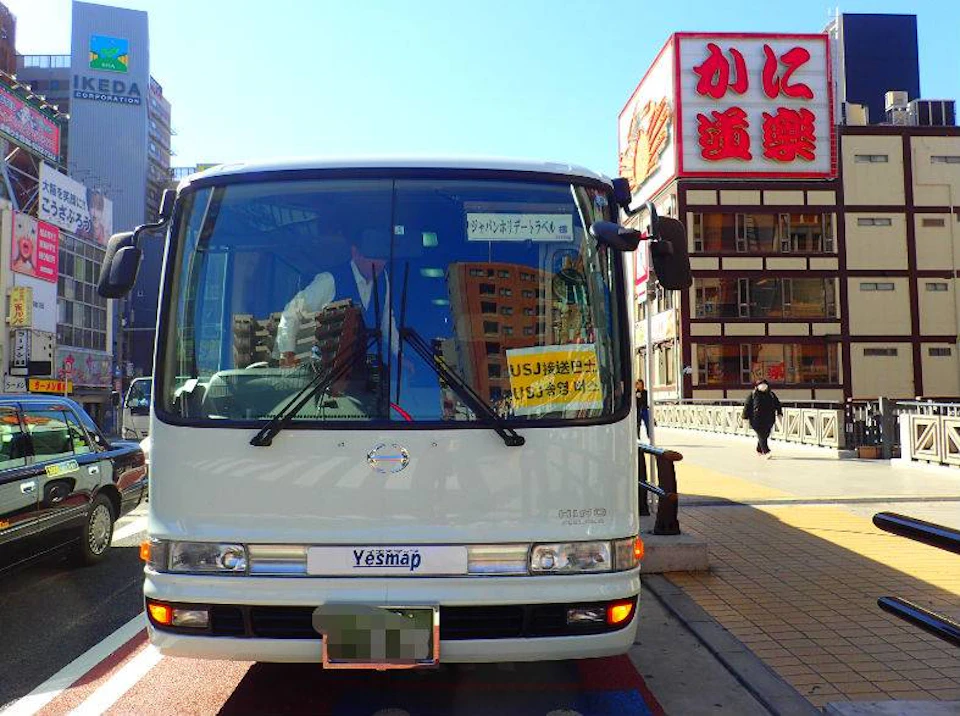 A white bus parked on a city street with a large sign in Japanese visible on a nearby building.