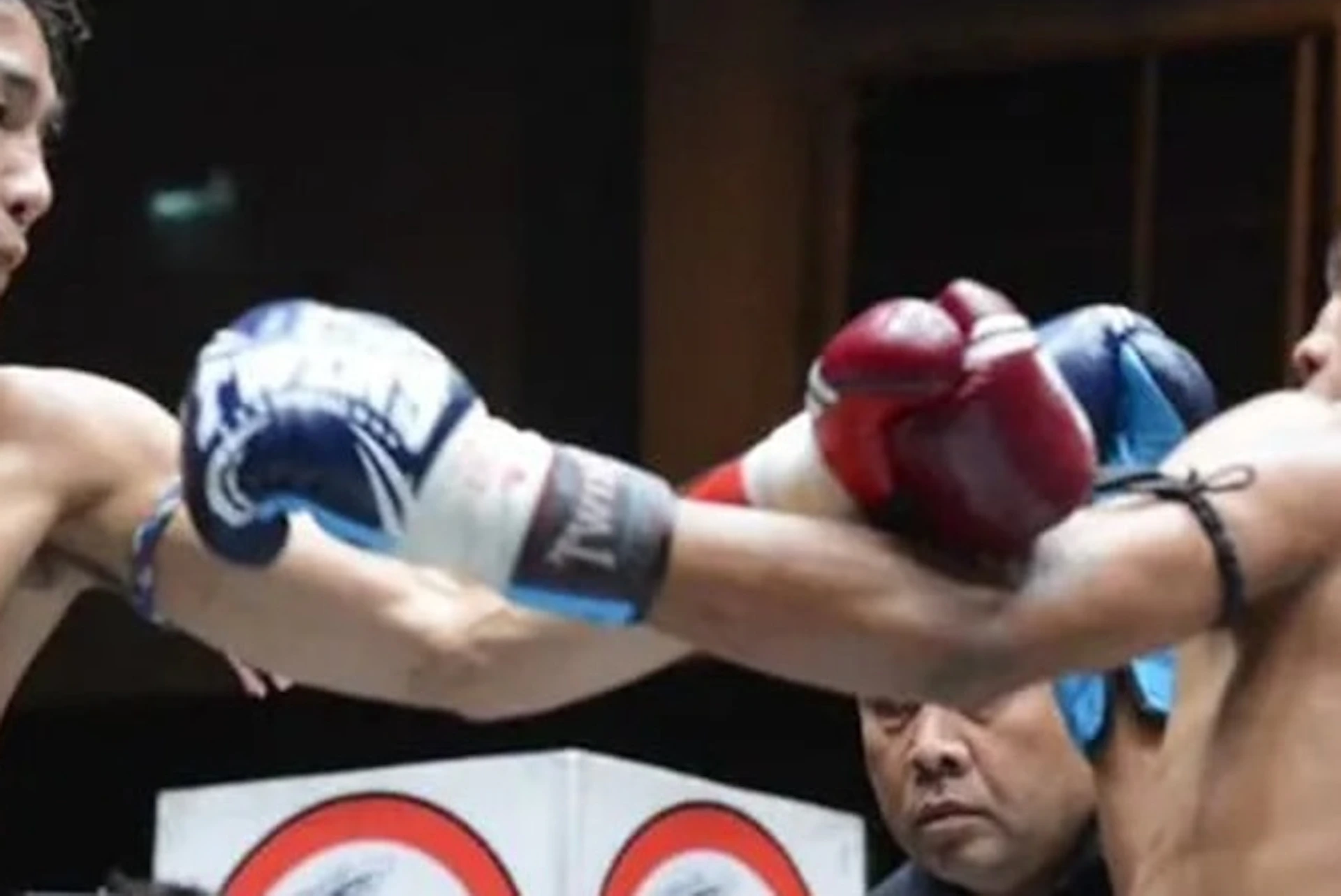 Two boxers in a ring exchanging punches during a match, with a referee and a cameraman in the background.