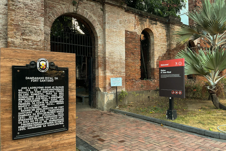 A historic brick archway with informational signs in front, including one about a shrine dedicated to Jose Rizal.