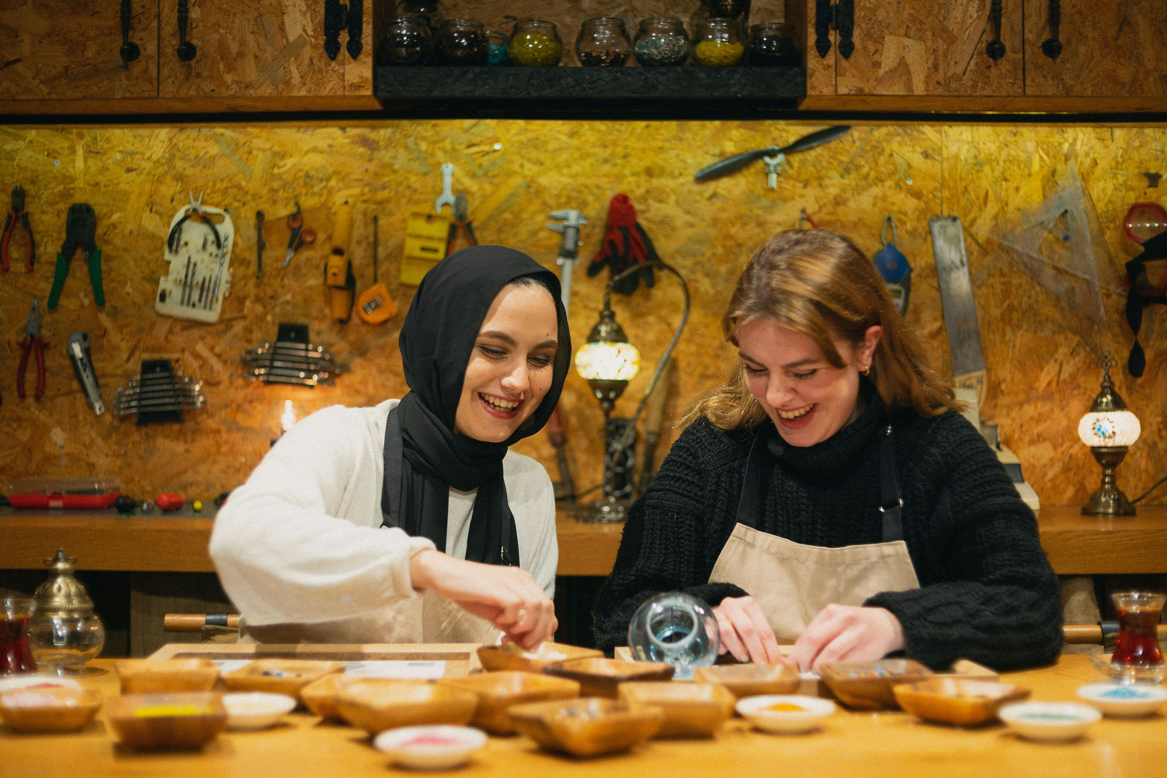 两位女士在车间里微笑着制作马赛克灯，周围都是工具。