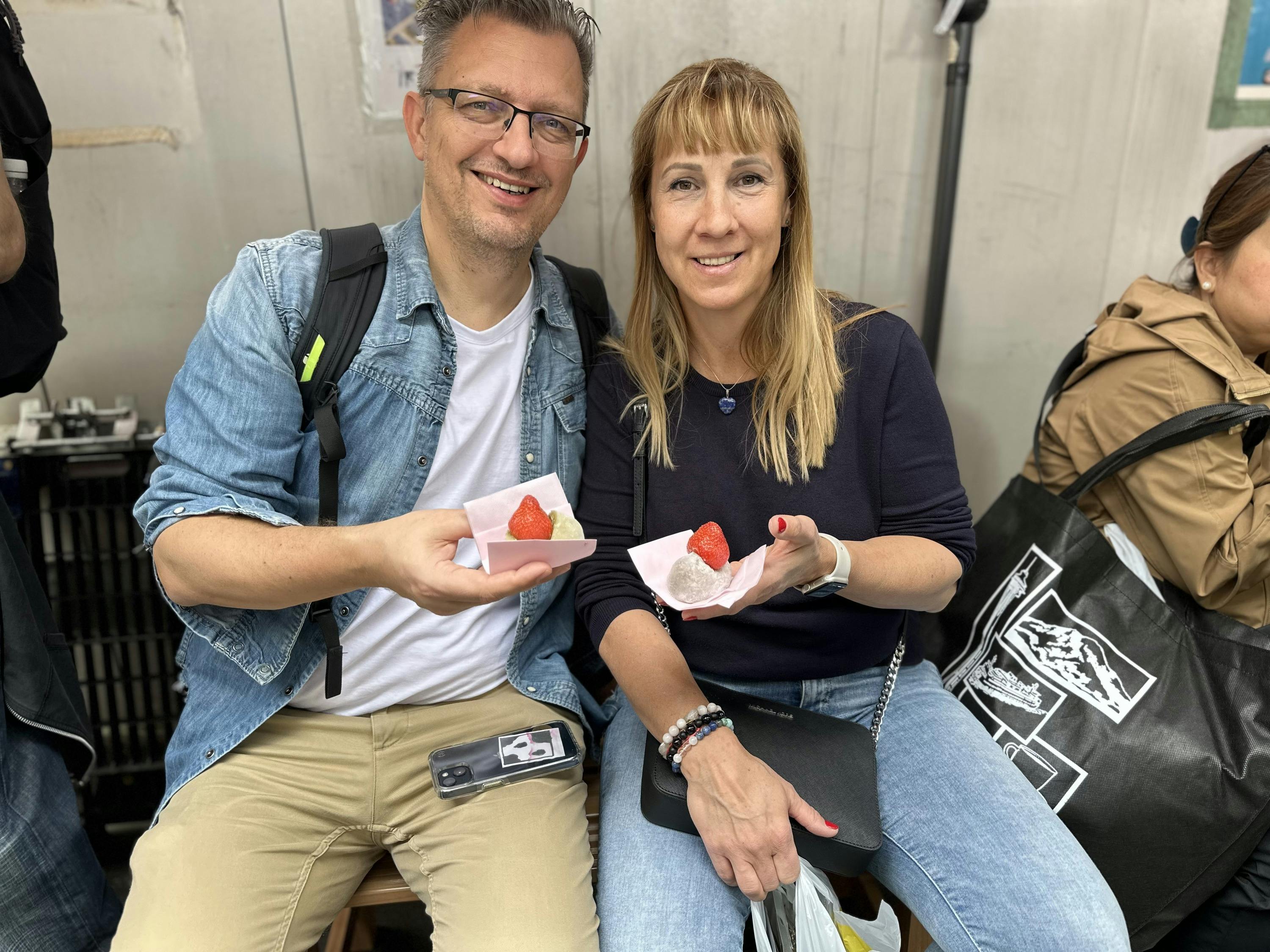 A man and a woman sitting together, each holding a dessert with a strawberry on top, smiling at the camera.