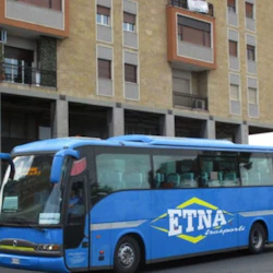 A blue bus with the text 'ETNA trasporti' parked in front of a beige building with multiple balconies and windows.