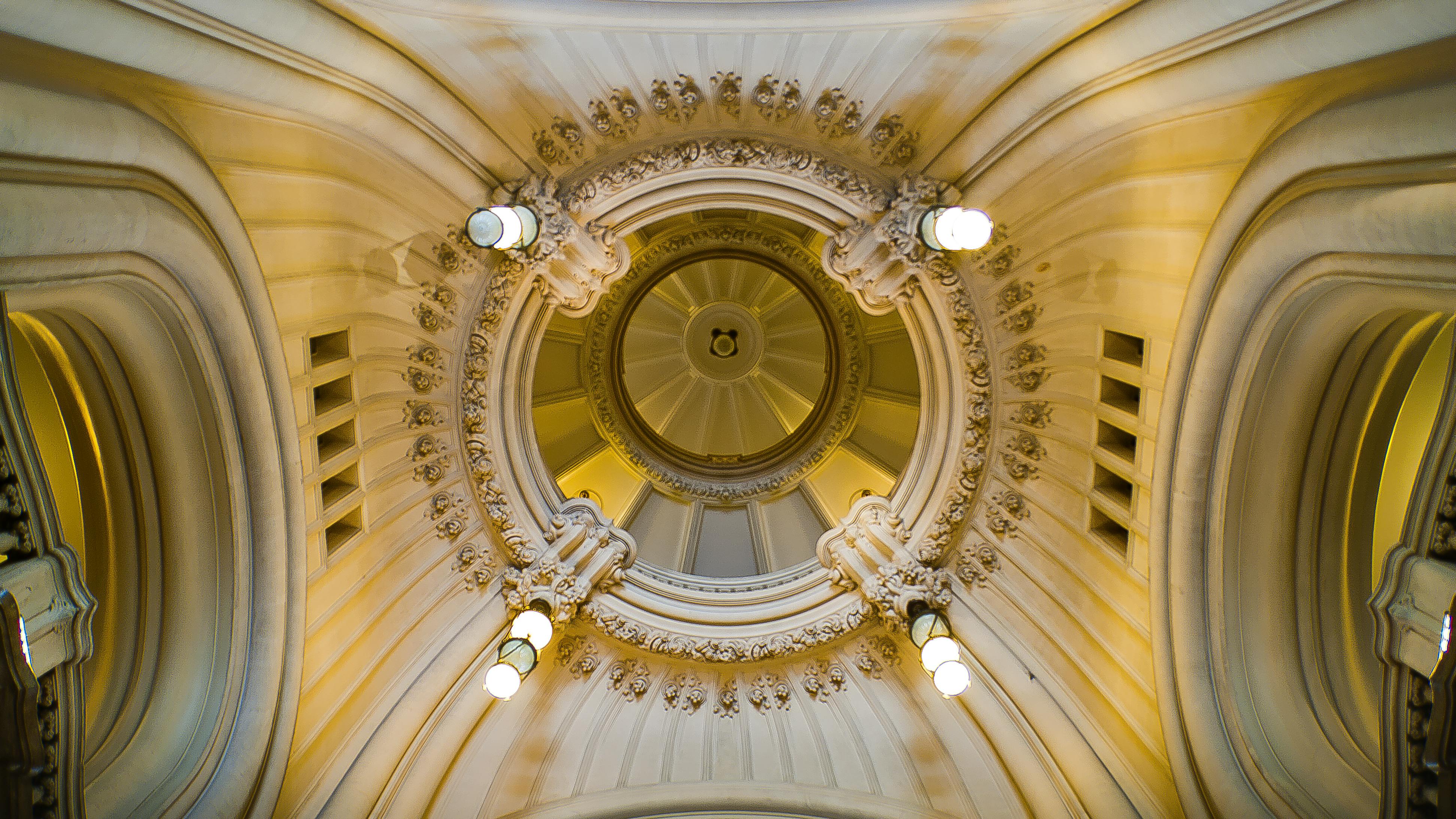 Ornate domed ceiling with intricate moldings and symmetrical light fixtures.