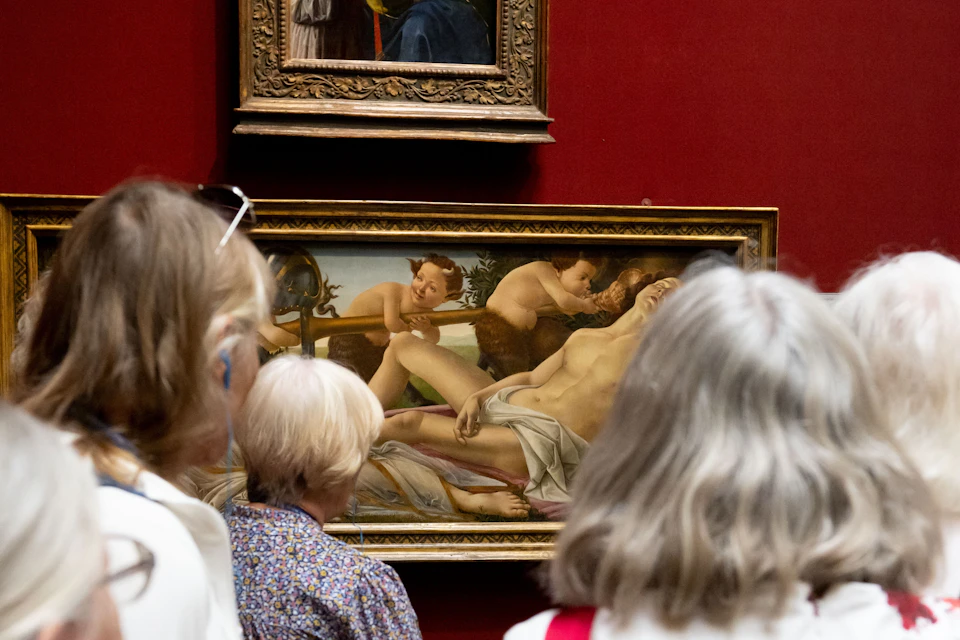 A group of people observing a classical painting in a museum. The artwork depicts mythological figures.
