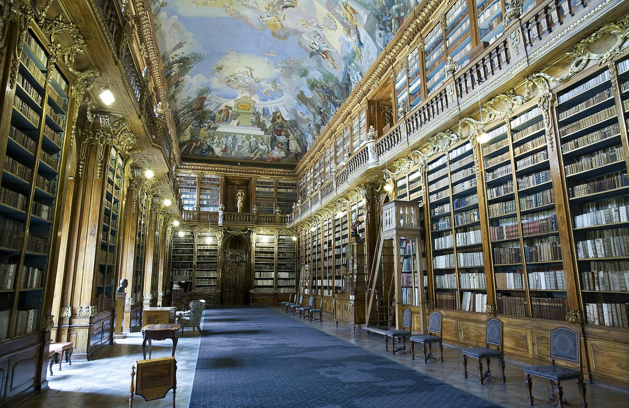 高い木製の本棚、華やかな装飾、塗装された天井、青いカーペットの通路がある豪華な図書館。