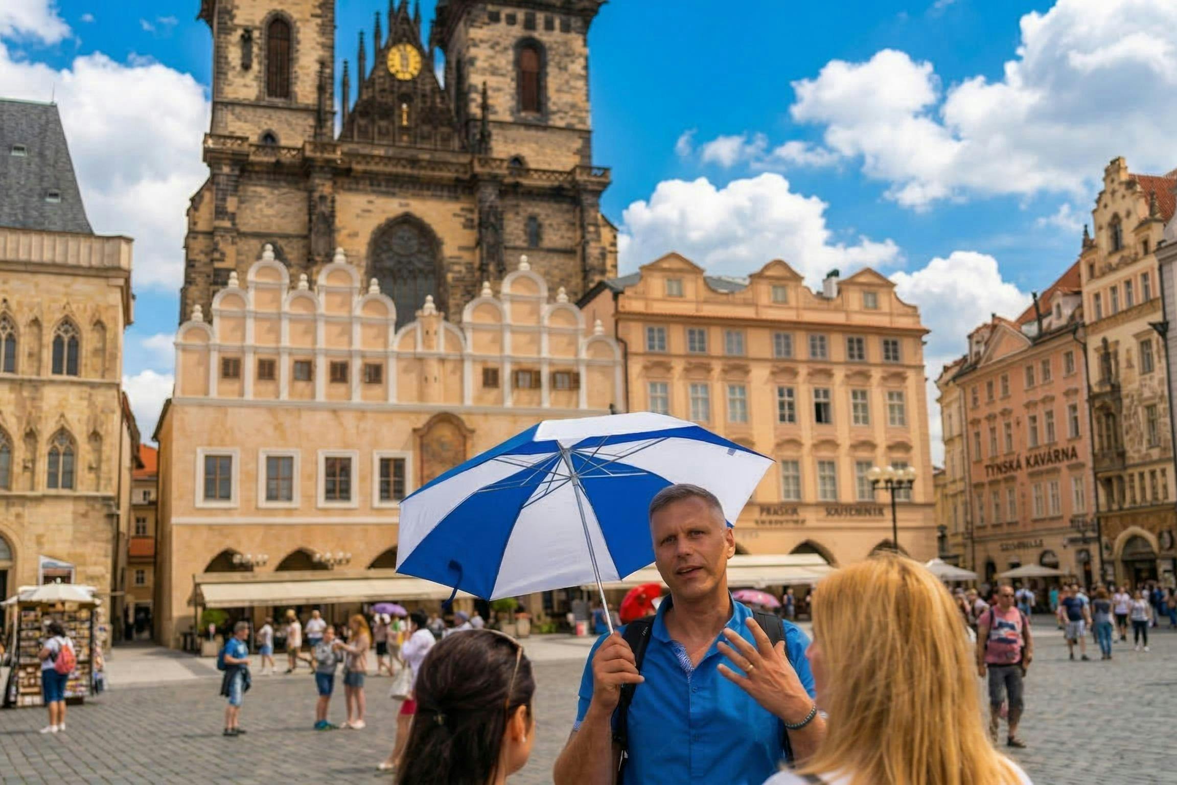 Un hombre con un paraguas azul y blanco habla con dos mujeres en una plaza europea con edificios históricos al fondo.