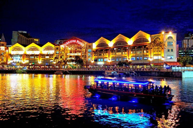 Budova na břehu řeky se v noci rozsvítila a odrazila se ve vodě. V popředí pluje loď s modrými světly.