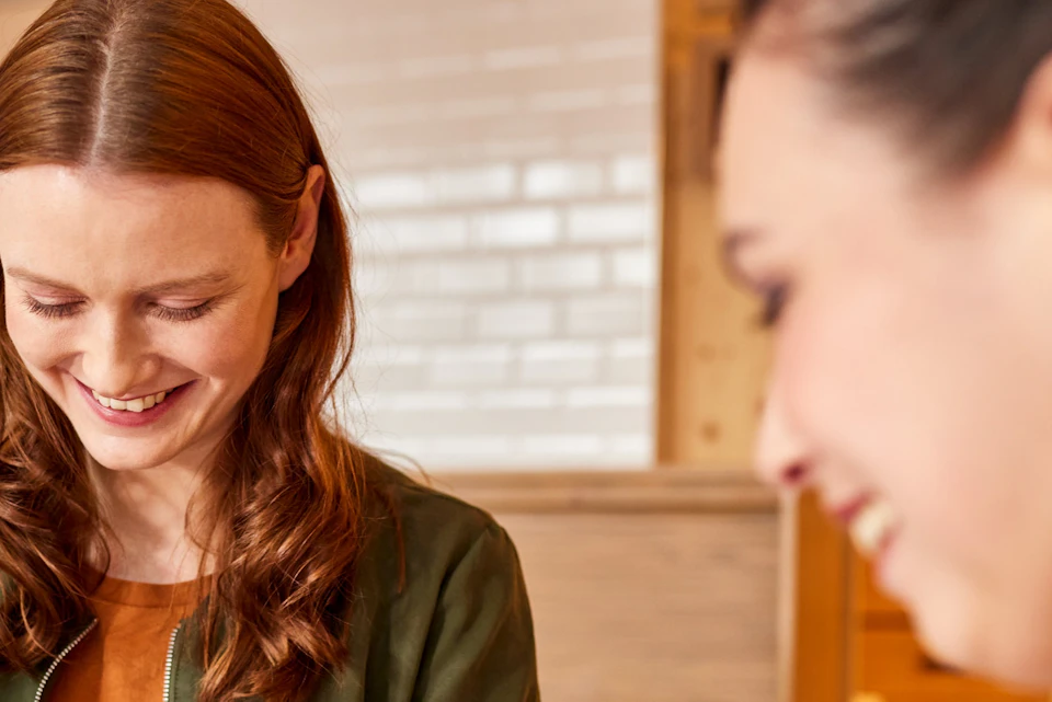 Two women decorating chocolate bars with toppings in a kitchen, smiling and enjoying the activity.