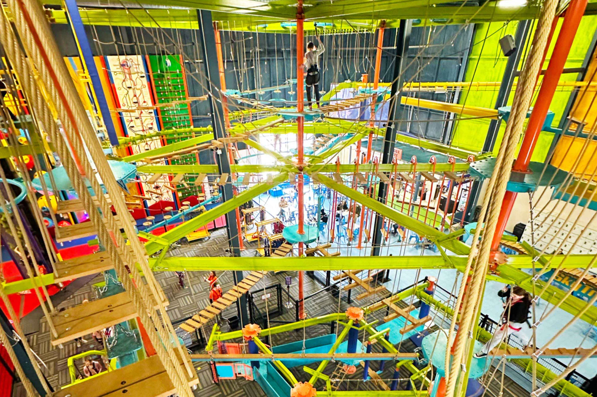 An indoor adventure course with multiple levels of ropes, ladders, and platforms, featuring bright green and orange structures.