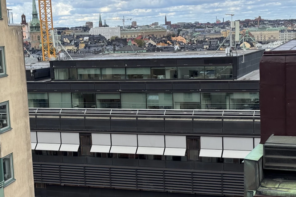 A view of a modern building with large windows and awnings, set against a cityscape of rooftops and distant spires.
