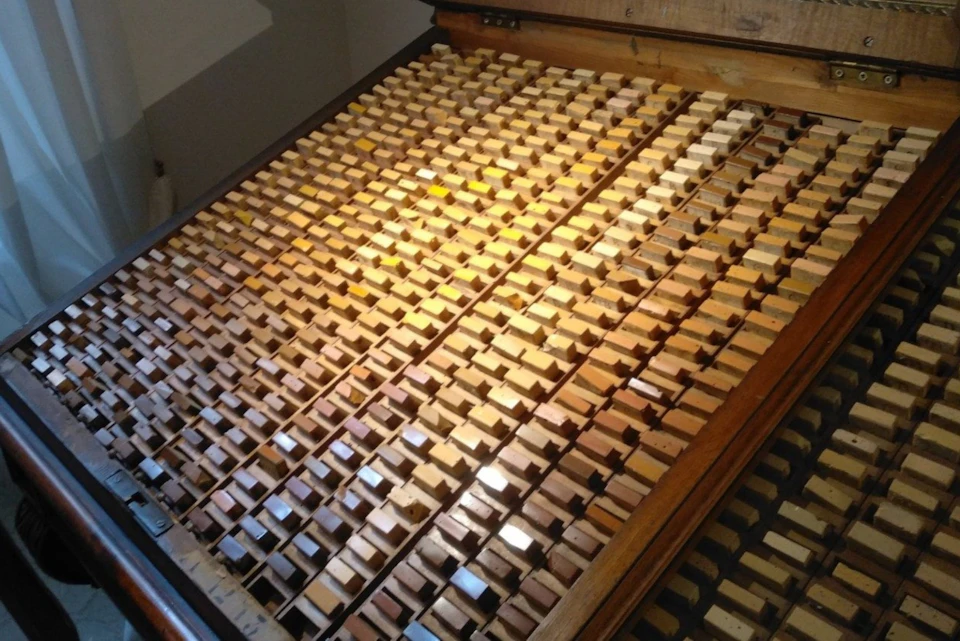 A wooden drawer filled with numerous small rectangular pieces arranged in a grid, resembling a collection of tiles or samples.