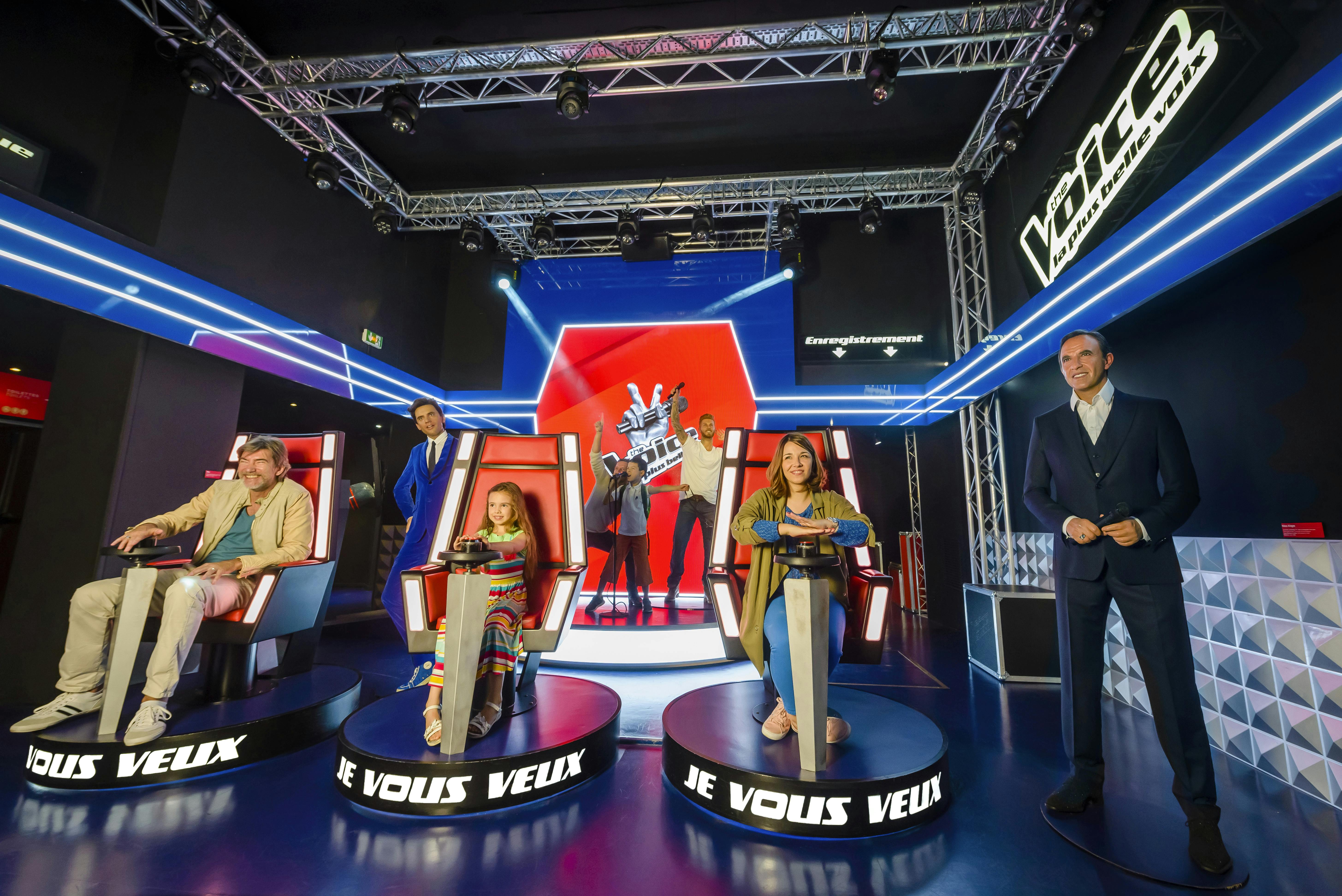 Lidé pózující na výstavě na téma „Hlas“ se dvěma jedinci v červených židlích a voskovou figurínou muže v obleku.