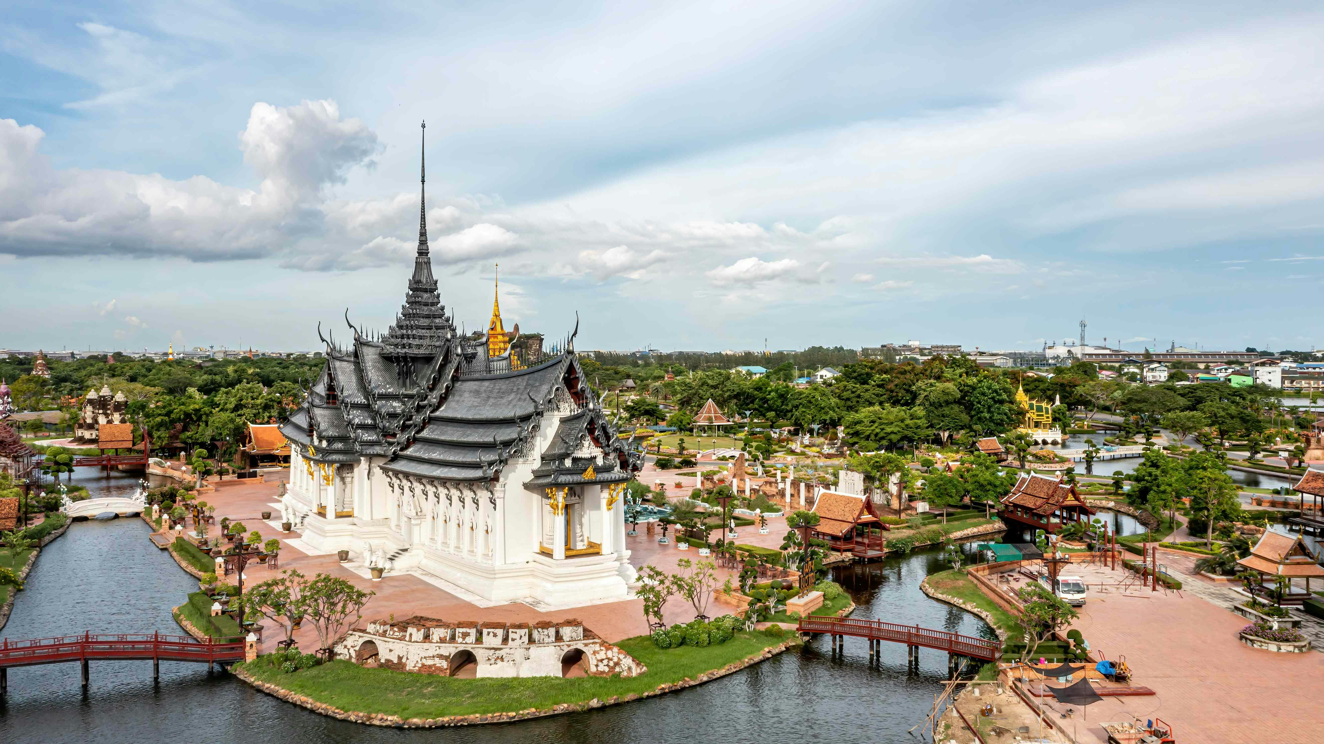 Luftaufnahme eines thailändischen Tempels mit komplizierter Überdachung, umgeben von Wasser und Brücken, inmitten von üppigem Grün und verschiedenen Strukturen.