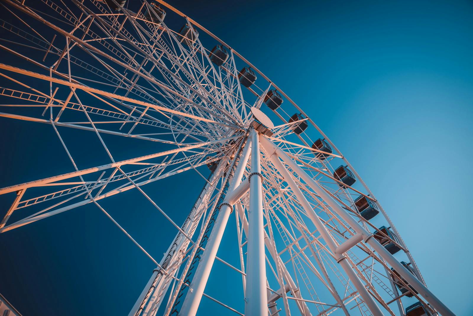 Close-up of a Ferris wheel against a clear blue sky, highlighting its white metal framework and passenger cabins.