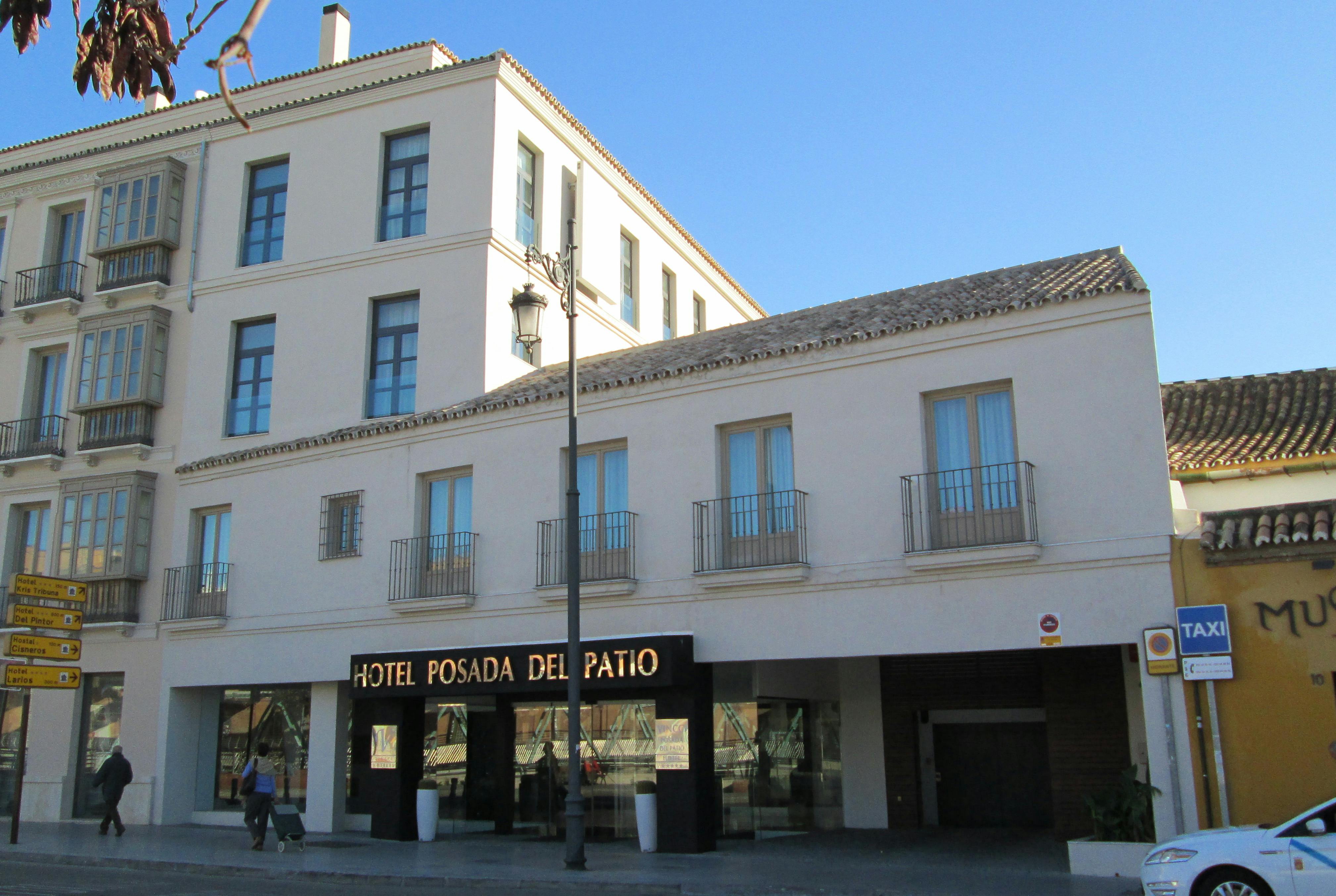 クリーム色の建物の外観には、複数の窓、バルコニー、入り口の近くに「Hotel Posada del Patio」と書かれた看板があります。