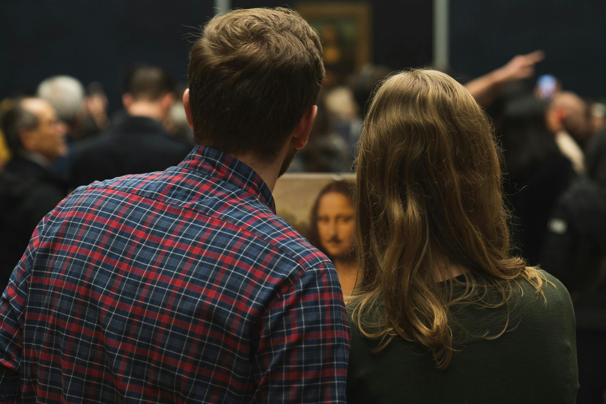 Un homme et une femme vus de dos observent le tableau de Mona Lisa dans un musée bondé.