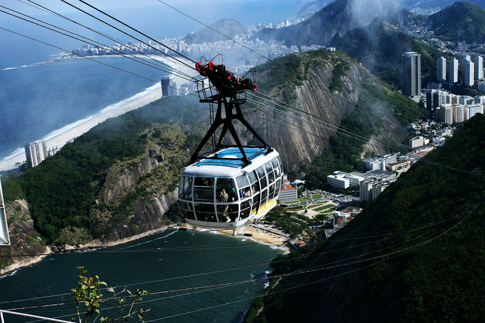 A cable car suspended over a coastal city, with mountains, buildings, and the ocean visible in the background.