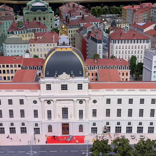 Modell av en europeisk stad med en framträdande klassisk byggnad, röda takkonstruktioner och små figurer på gator och trottoarer.