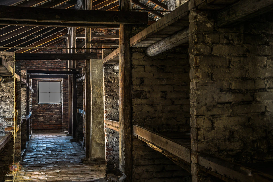 Interior of an old brick building with wooden beams and shelves, featuring a small window and a stone floor.