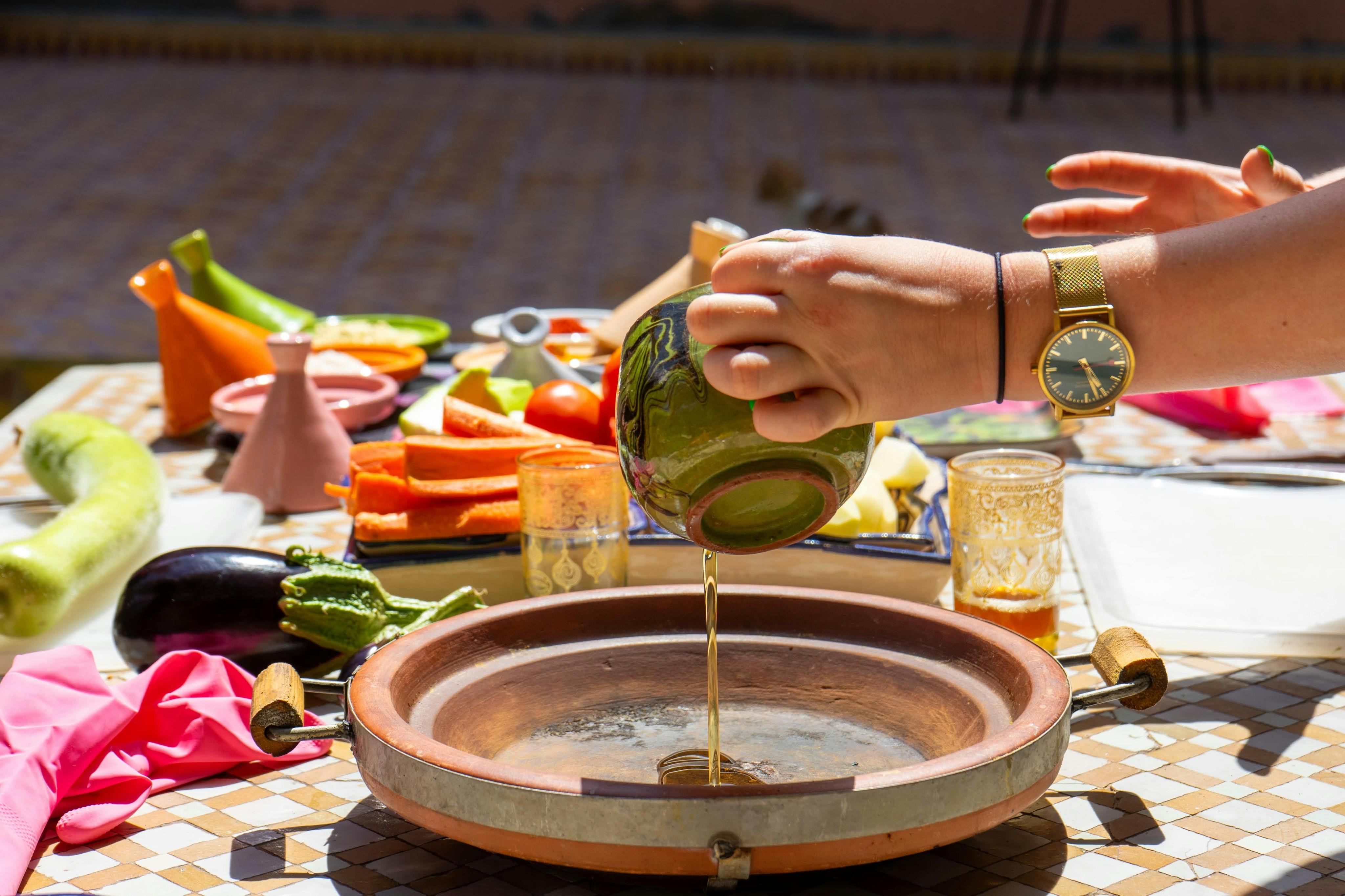 屋外で様々な切り野菜や調味料をセットしたテーブルの上に置かれた粘土皿にオイルを手で注ぎます。