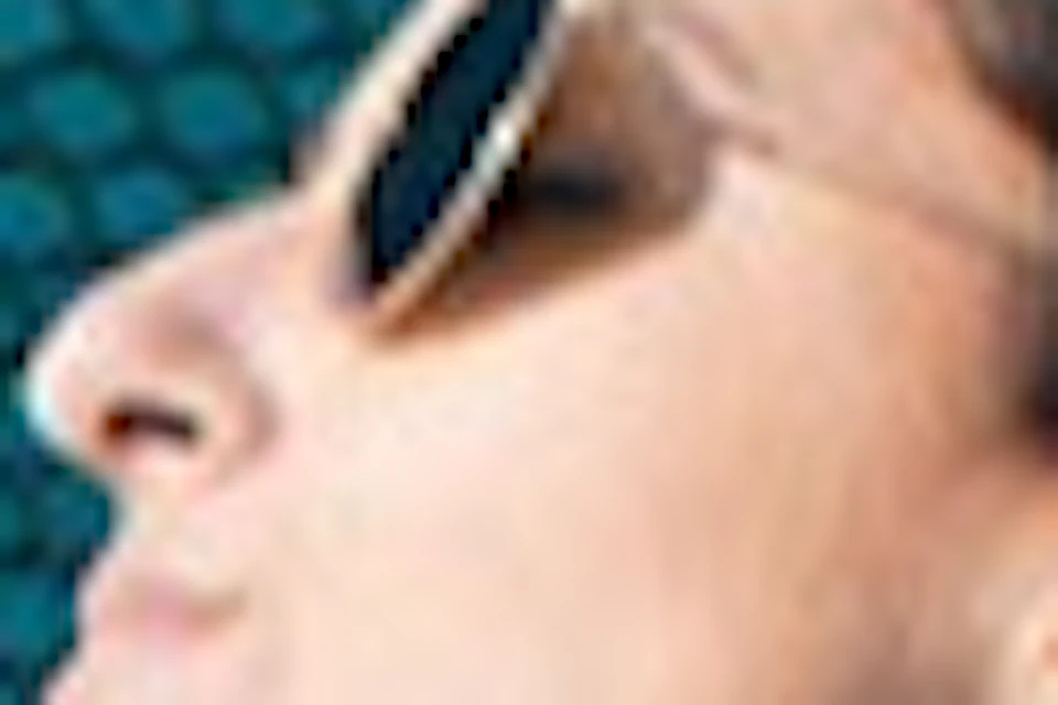 A woman in a swimsuit and sunglasses relaxes on a blue hammock under the sun.