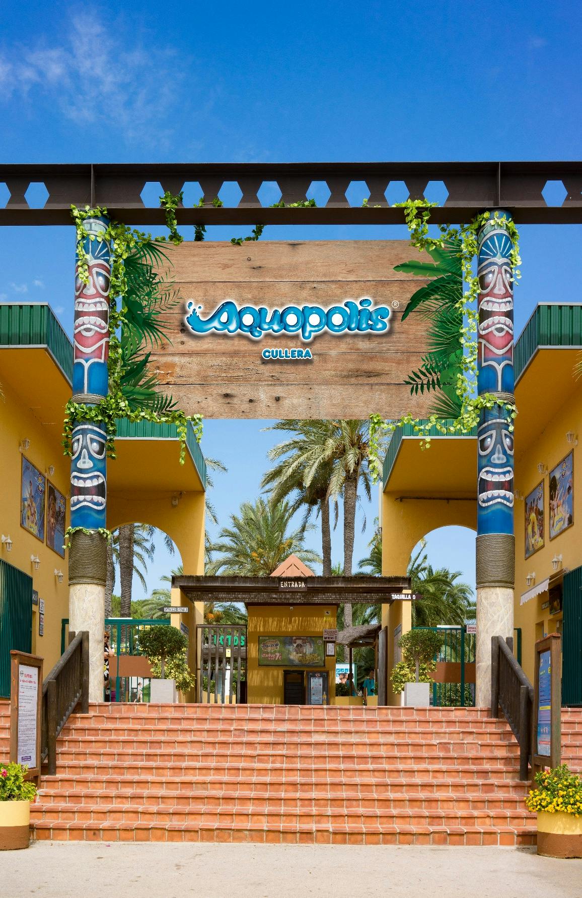 Entrance to Aquopolis aquatic park, featuring tiki-themed columns, palm trees, and signs. Red brick steps lead to the ticket area.