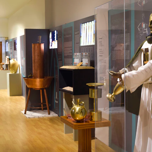 Museumsutställning med historiska artefakter, inklusive en staty, kopparkärl och informationsskärmar på ett trägolv.