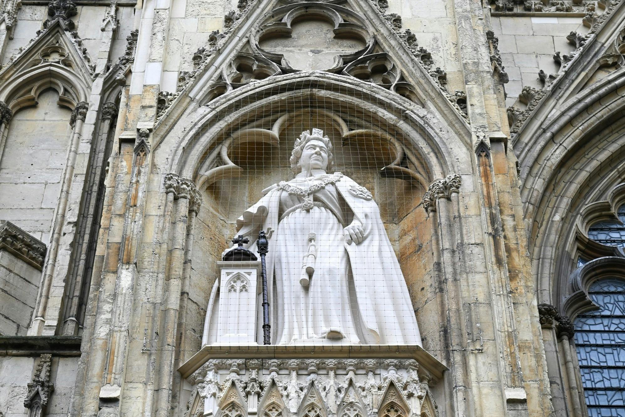 ゴシック建築のニッチの中にある、王室の服装をした歴史的な人物の石像。ネットに包まれています。