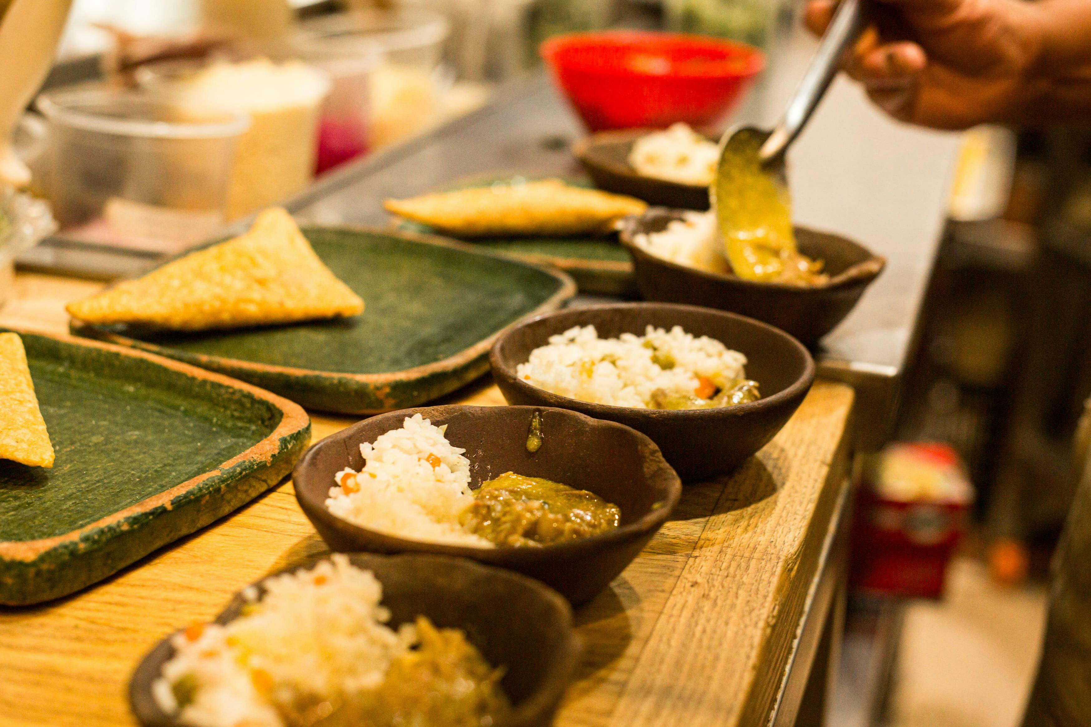 Ciotole di riso e salsa verde in preparazione, con piatti e alimenti su un bancone di legno.