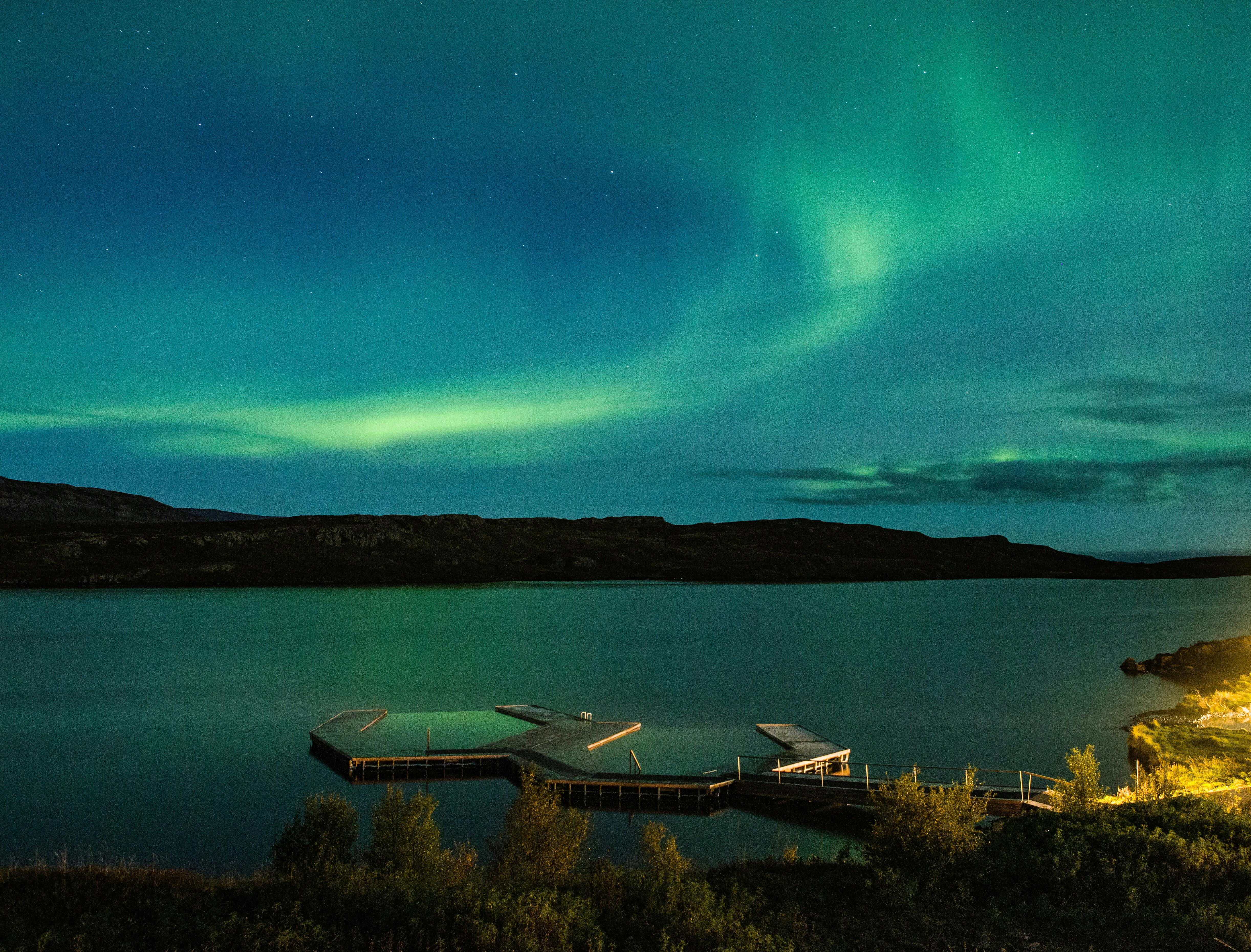 一个宁静的湖泊，一个木制码头延伸到水中，北极光照亮了上面的天空。