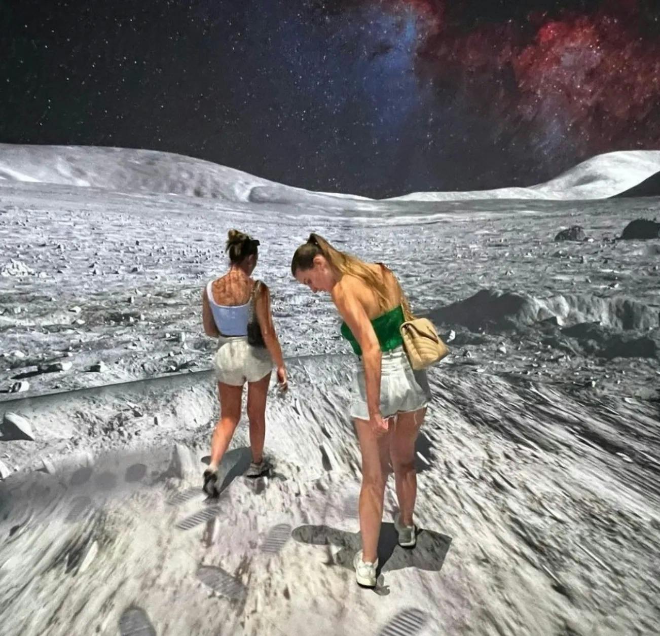 Twee vrouwen in nonchalante zomeroutfits lopen over een maanachtig landschap met op de achtergrond een sterrenhemel.