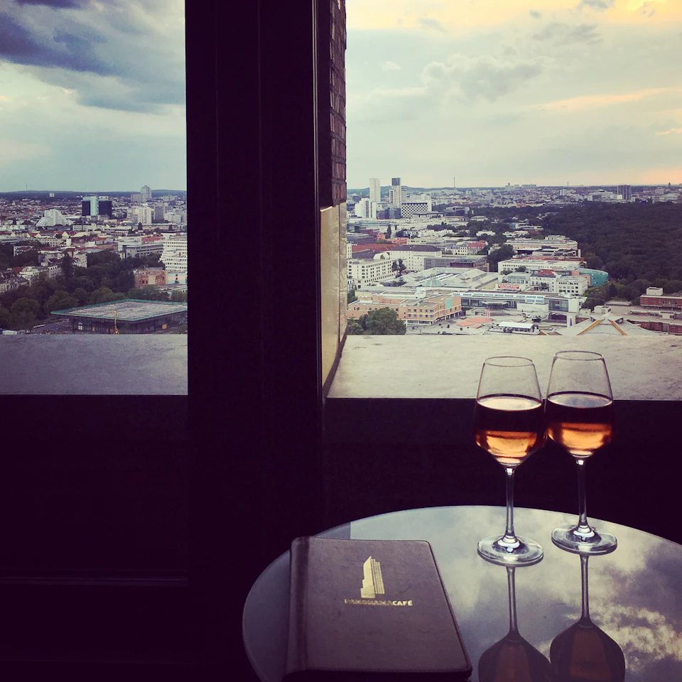 Two glasses of wine and a menu on a table overlooking a cityscape at twilight through a large window.