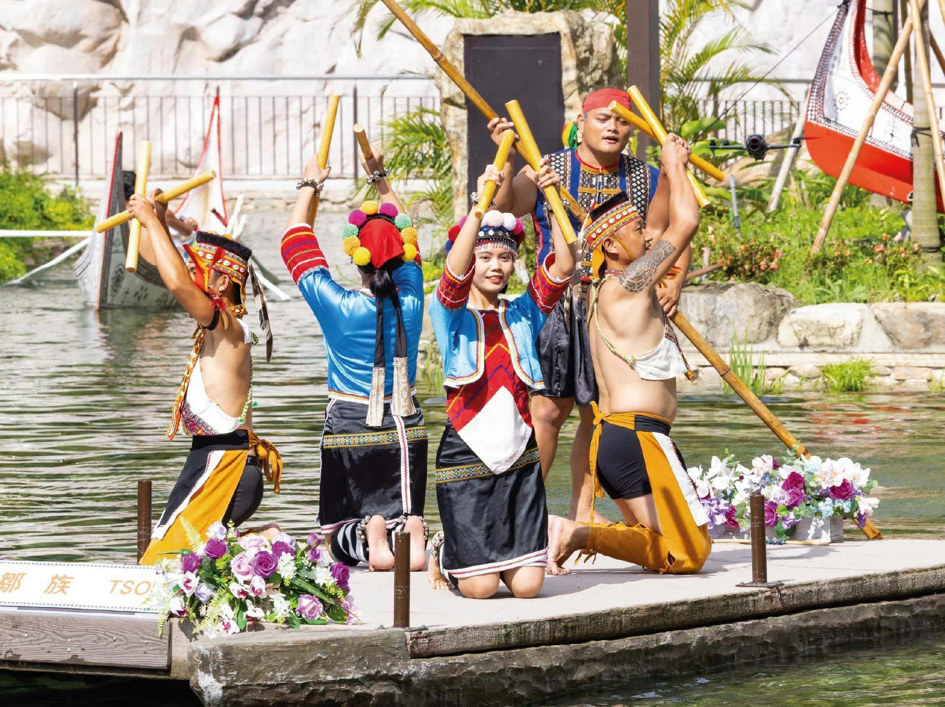 A group of people in traditional attire performing a cultural dance on a wooden raft decorated with flowers.