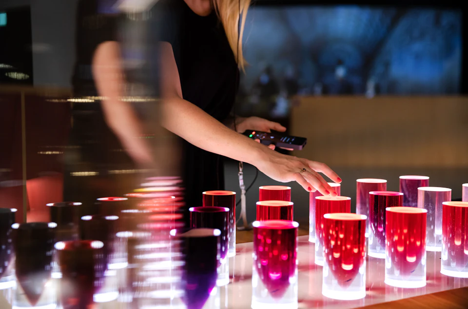 A person touching glowing, cylindrical objects of varying shades of red and pink in a dimly lit room.