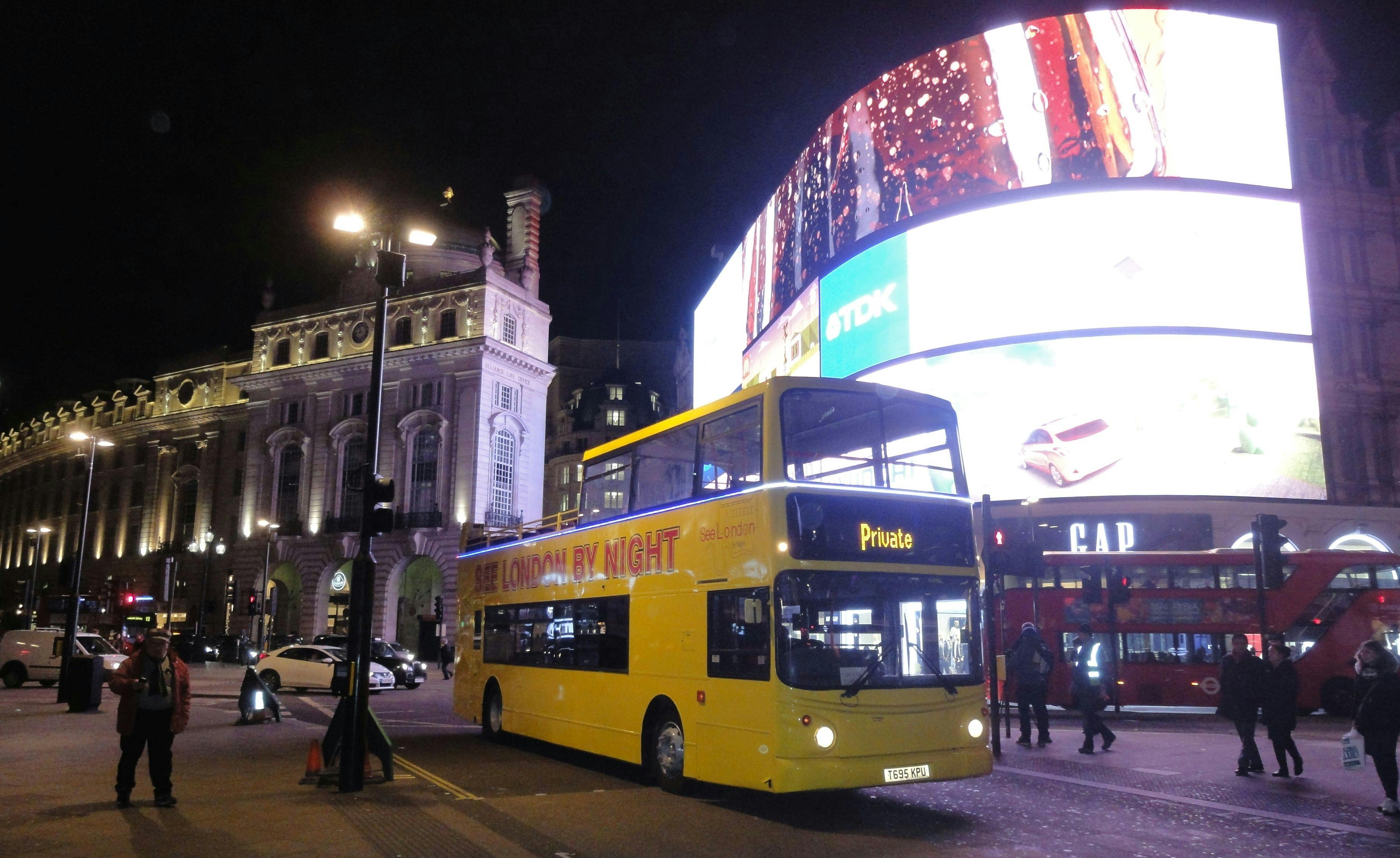 Żółty piętrowy autobus z etykietą „See London By Night” w pobliżu oświetlonych budynków i dużych cyfrowych billboardów w nocy.