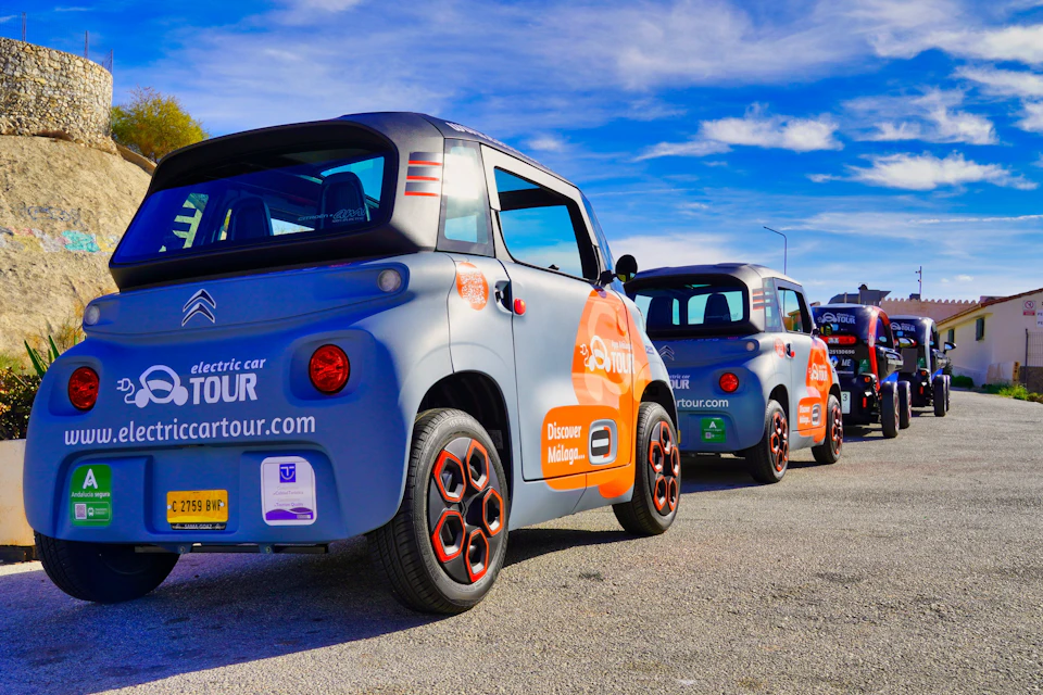 Several compact electric cars parked in a row on a sunny day, each displaying advertising for a city tour service.