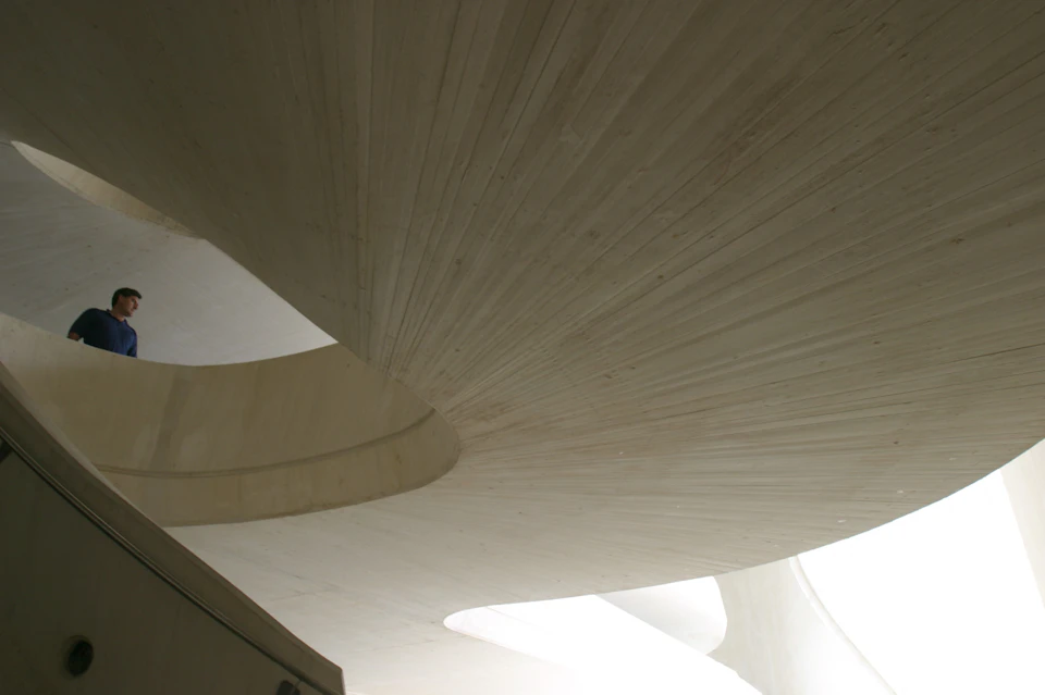 Curved, light-colored concrete structure with a modern architectural design, featuring smooth lines and intersecting planes.