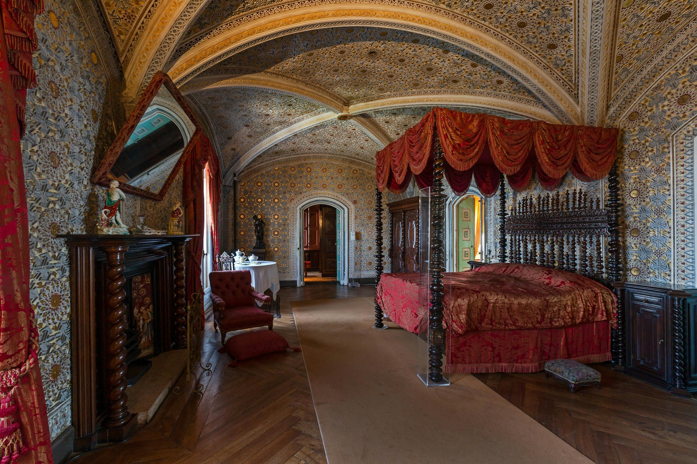 Camera da letto ornata con letto a baldacchino, soffitto a volta decorato, camino e mobili antichi in un ambiente storico.
