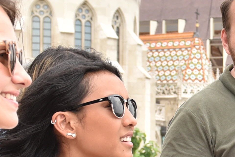 Three people outdoors, talking and smiling near a historic building with Gothic architecture and tiled roofs.