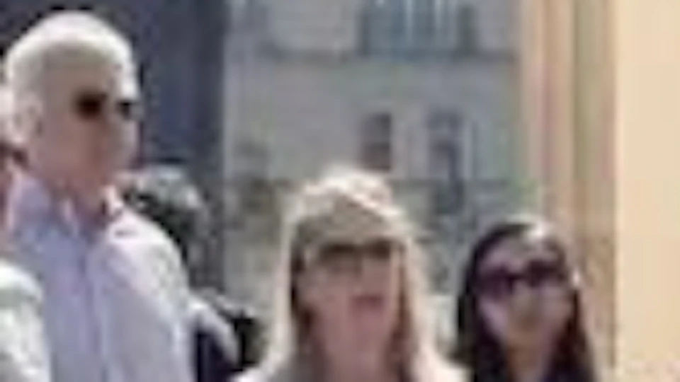 A tour guide points ahead while a group of tourists listens, standing in front of a large ornate building with pillars.