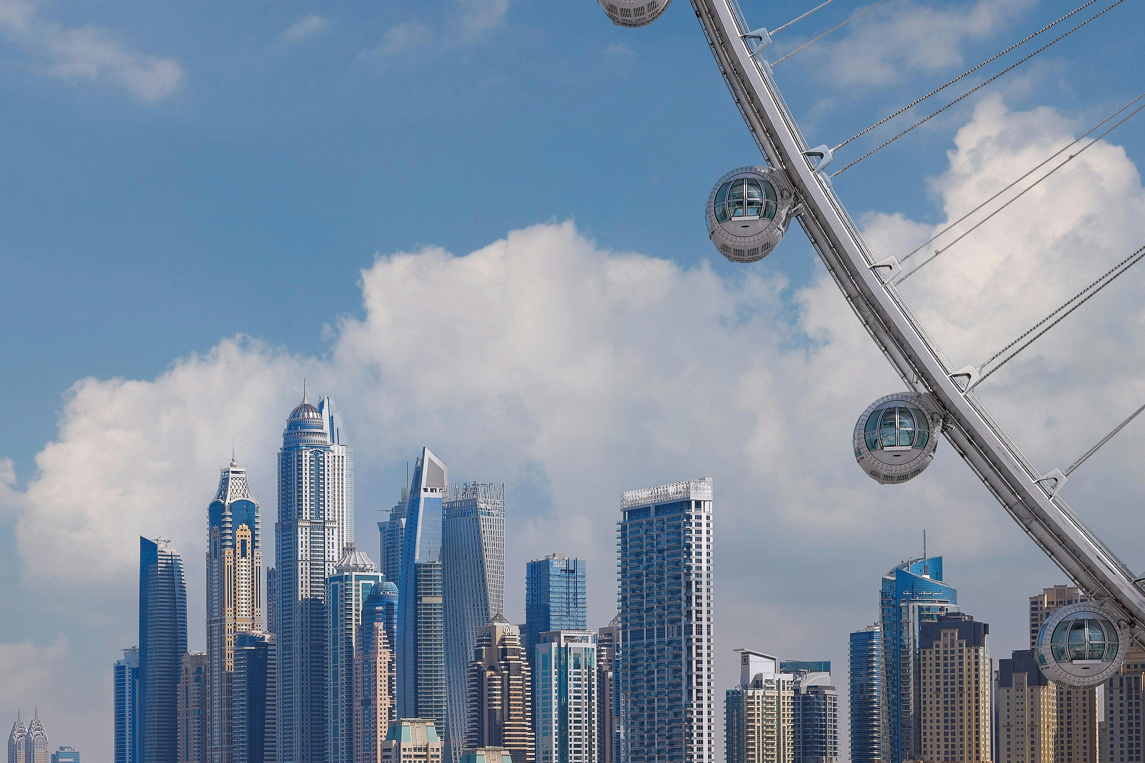 雲のある青い空の下にある近代的な高層ビルのスカイライン。右側には観覧車の一部が見えます。