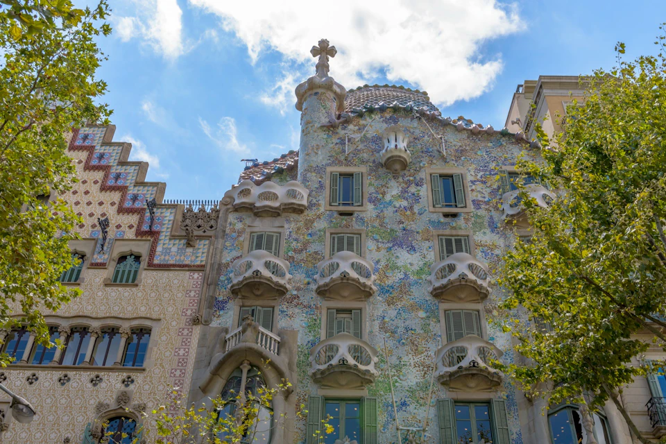 A colorful building with ornate architectural details, curved elements, and mosaic designs against a partly cloudy sky.