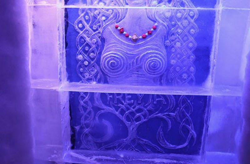 Ice carving of a woman with intricate hair, wearing a necklace. Text "FREYA" at the bottom, illuminated in blue light.