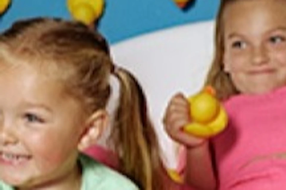 Two children sit in a bathtub filled with rubber ducks, surrounded by a blue room decorated with rubber ducks on the walls.