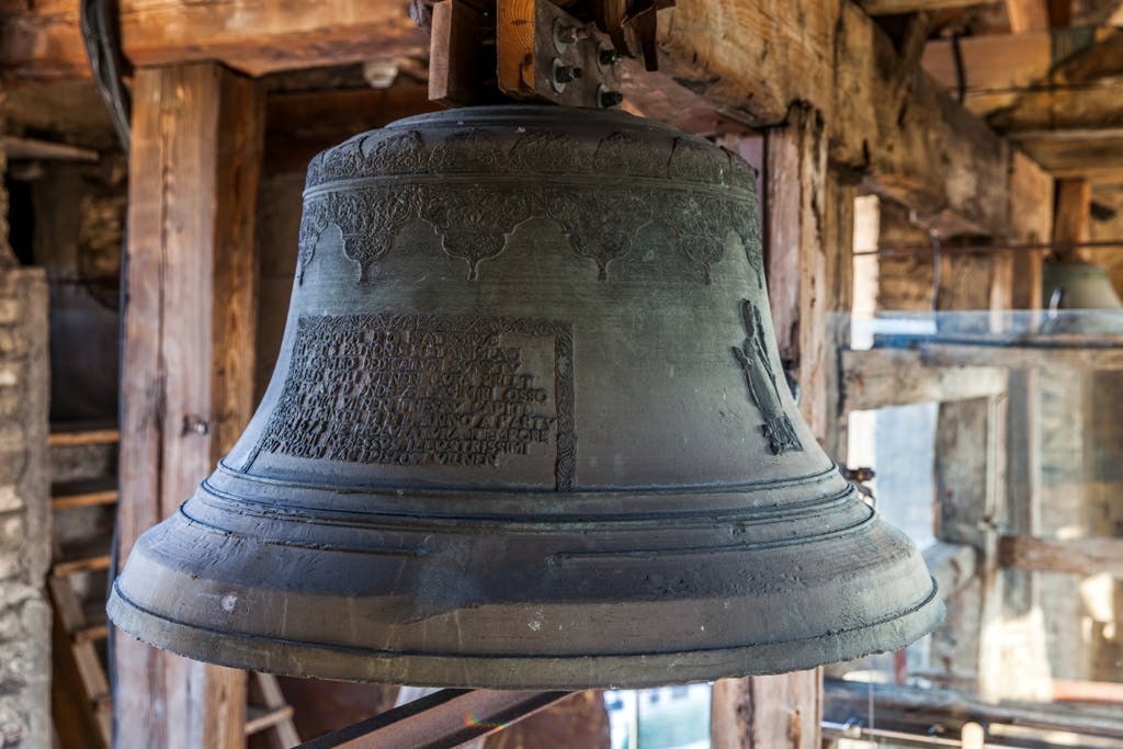 Large aged bronze bell with inscriptions and decorative patterns, hanging within a wooden bell tower.