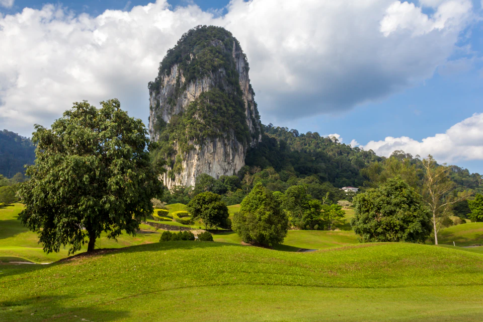 A large limestone hill covered in greenery surrounded by a scenic landscape of trees, grass, and rolling hills under a partly cloudy sky.