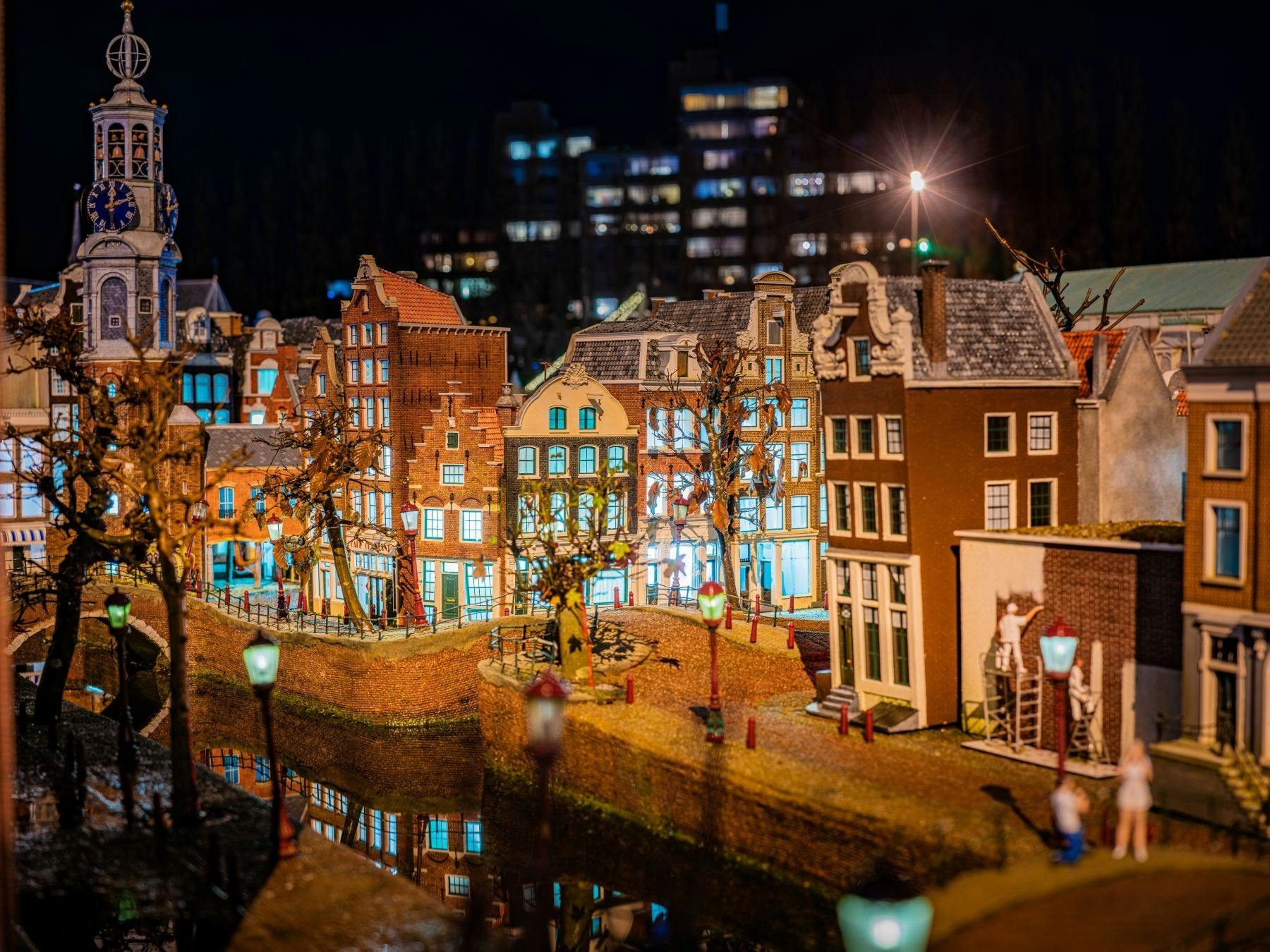 夜空を背景に、ライトアップされた詳細な建物、反射する運河、街灯を備えたミニチュア都市景観。