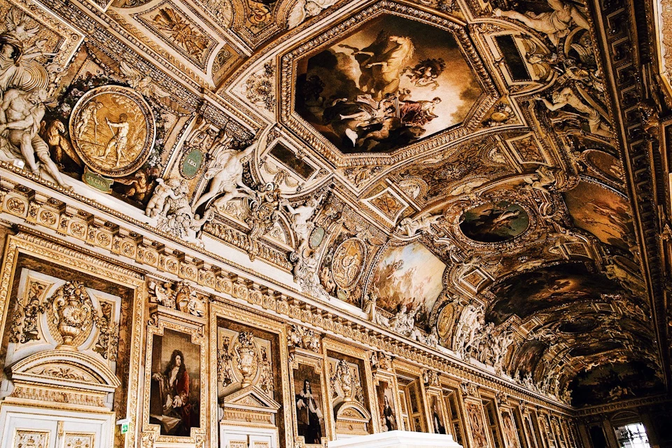 An ornate, golden room with detailed paintings, sculptures, and intricate designs covering the ceiling and walls.