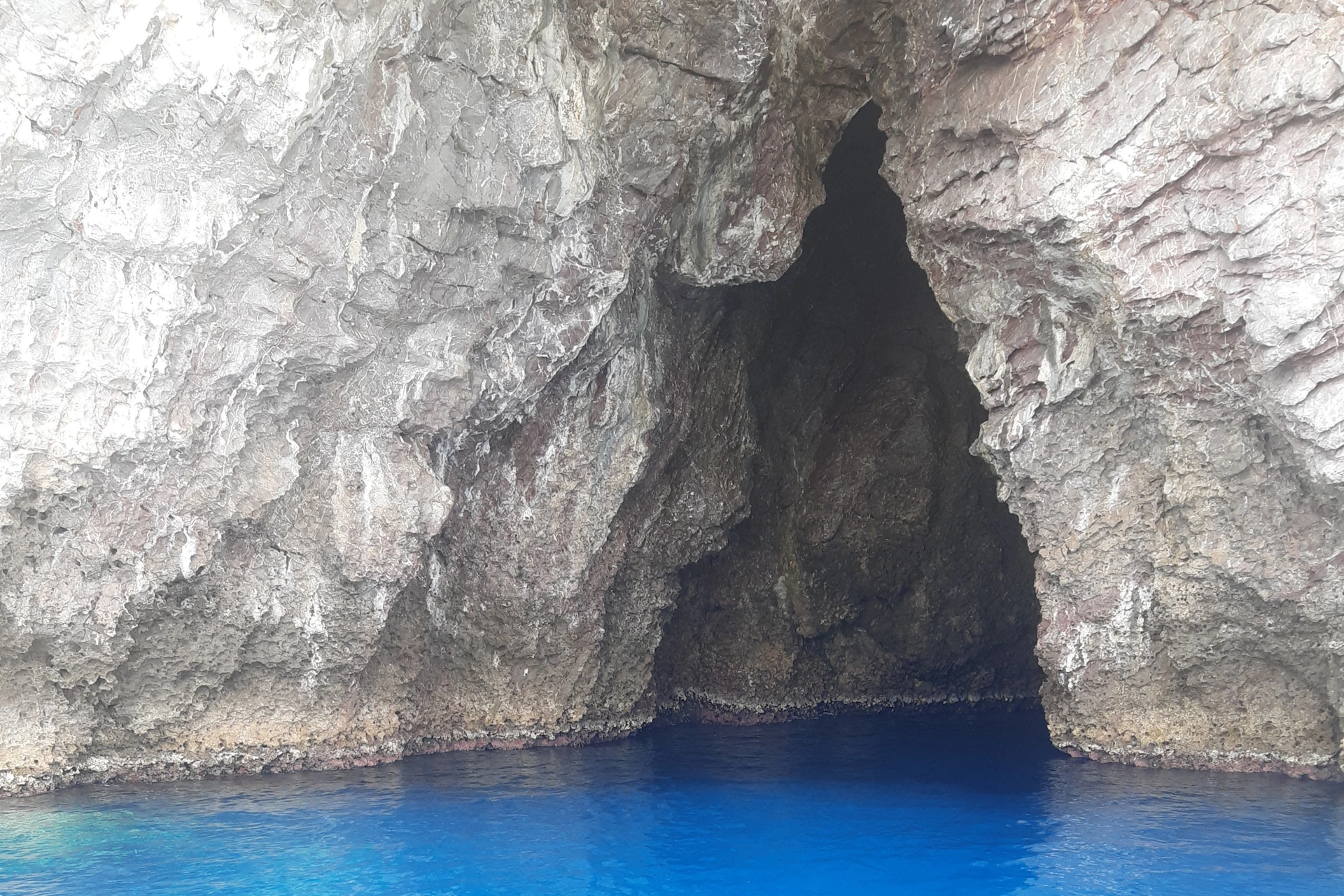 A rocky cave entrance with jagged edges, partially submerged in clear, bright blue water.